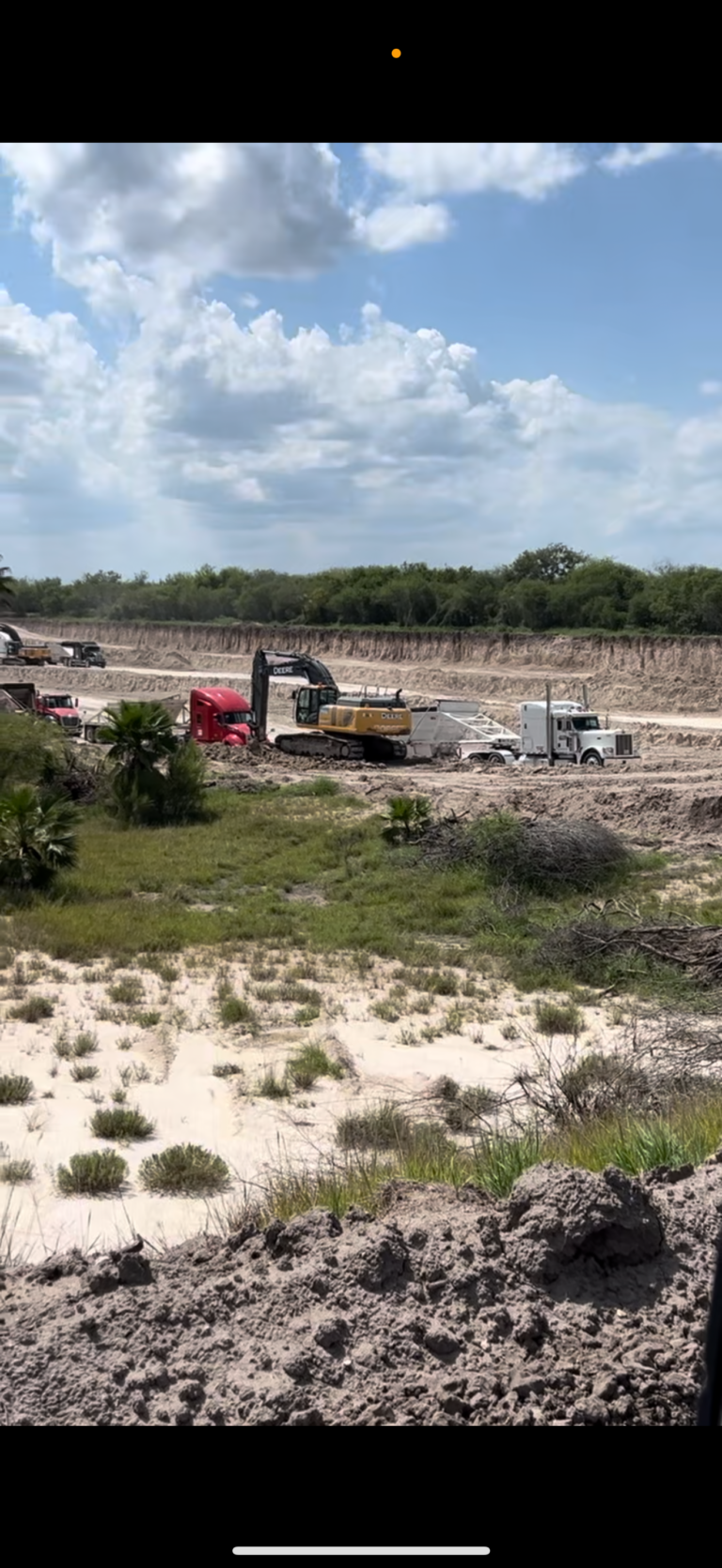 Excavator loading trucks inside a large dirt pit, capable of handling up to 20 yards of material in four scoops.